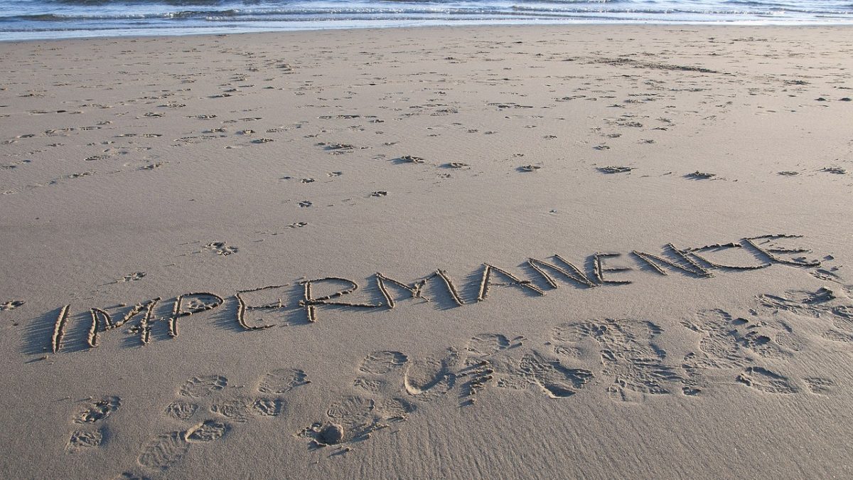 the word IMPERMENANCE written in the sand of an aesthetic beach.
